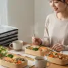 笑顔で宅食を食べる日本の若い女性と、テーブルに並べられた複数の宅食弁当