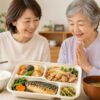 日本人の高齢女性と家族が減塩宅配弁当を囲み、健康的な食事を楽しむ様子