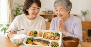 日本人の高齢女性と家族が減塩宅配弁当を囲み、健康的な食事を楽しむ様子